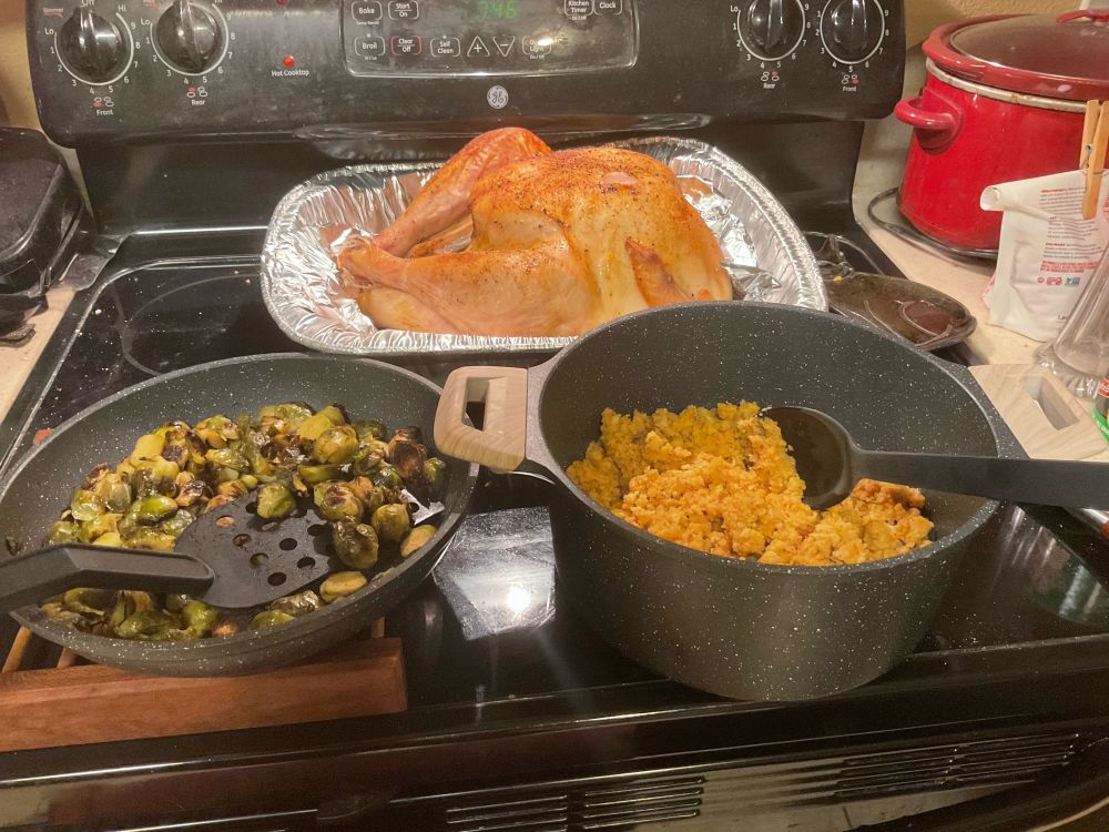 Sautéed Brussels sprouts, cornbread dressing, and roast turkey sitting on the stovetop. 