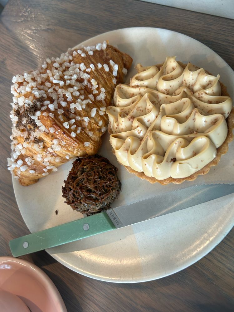 A plate with a macaroon, a tart, and a croissant and a knife 
