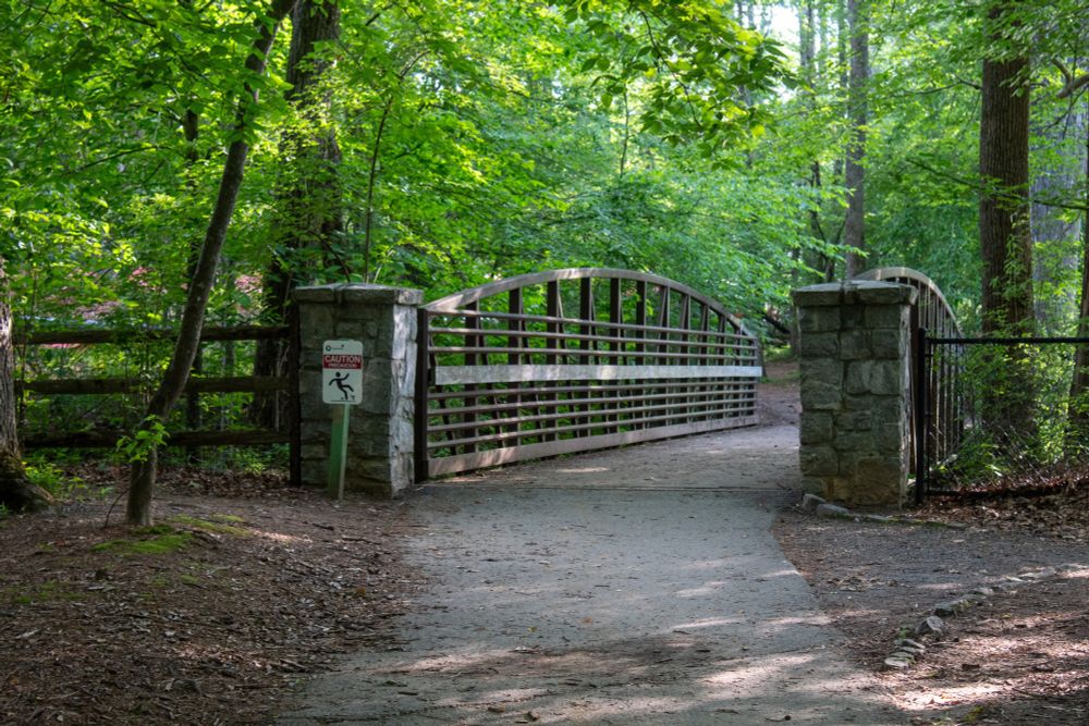 a metal bridge stretches across a path, leading into the forest
