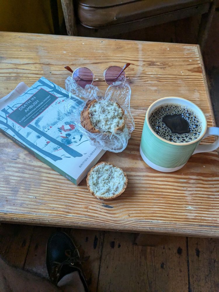 Coffee, muffin (Peach & Raspberry), book (Death in Ambush, Susan Gilruth), glasses. 