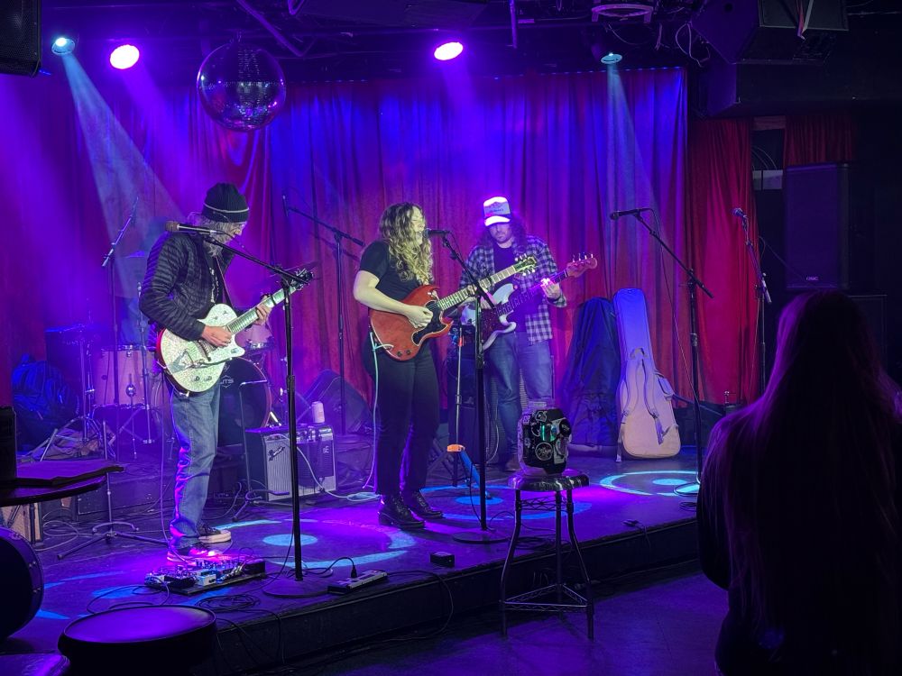 A band on stage at a club. A female singer playing guitar. a man playing guitar and another man playing bass