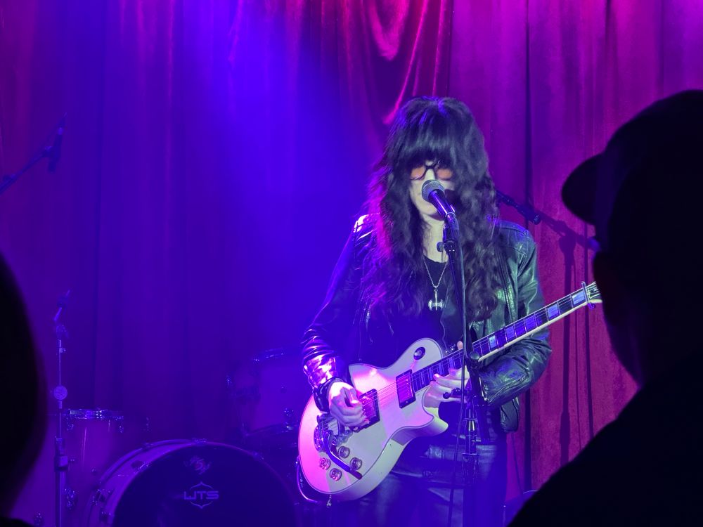 A female playing guitar and singing on stage at a bar. 