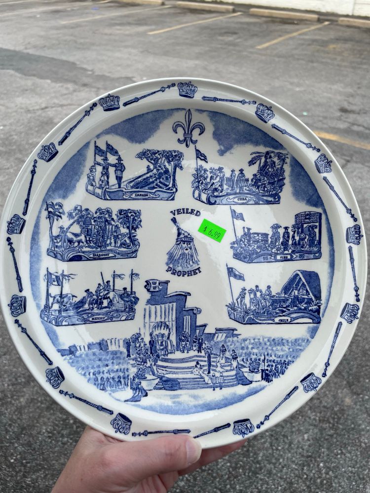 A white plate with blue drawings of various parade floats and ceremonies associated with St. Louis’s Veiled Prophet 