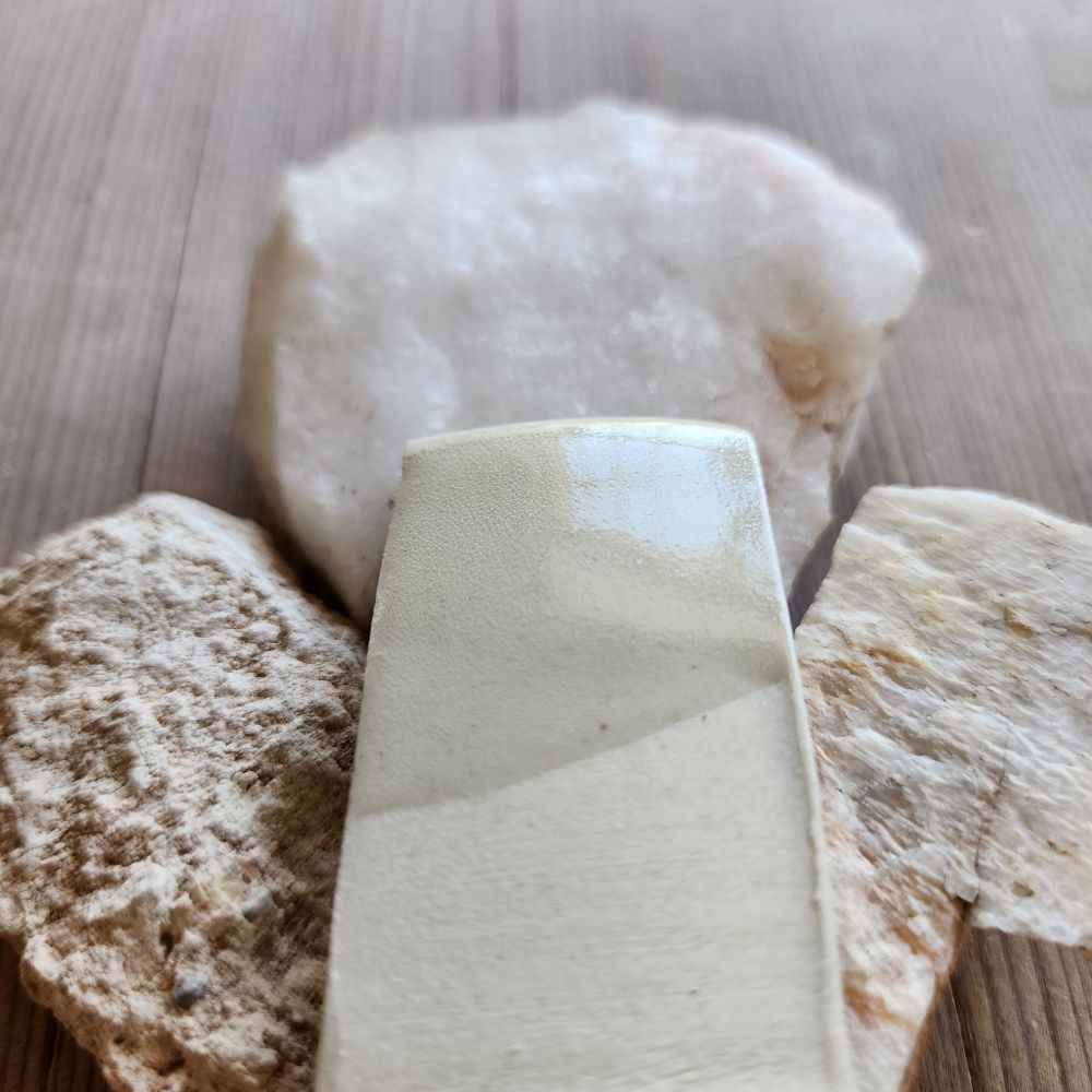 A porcelain test tiles showing a clear glaze made from the minerals and rock just behind the tile.