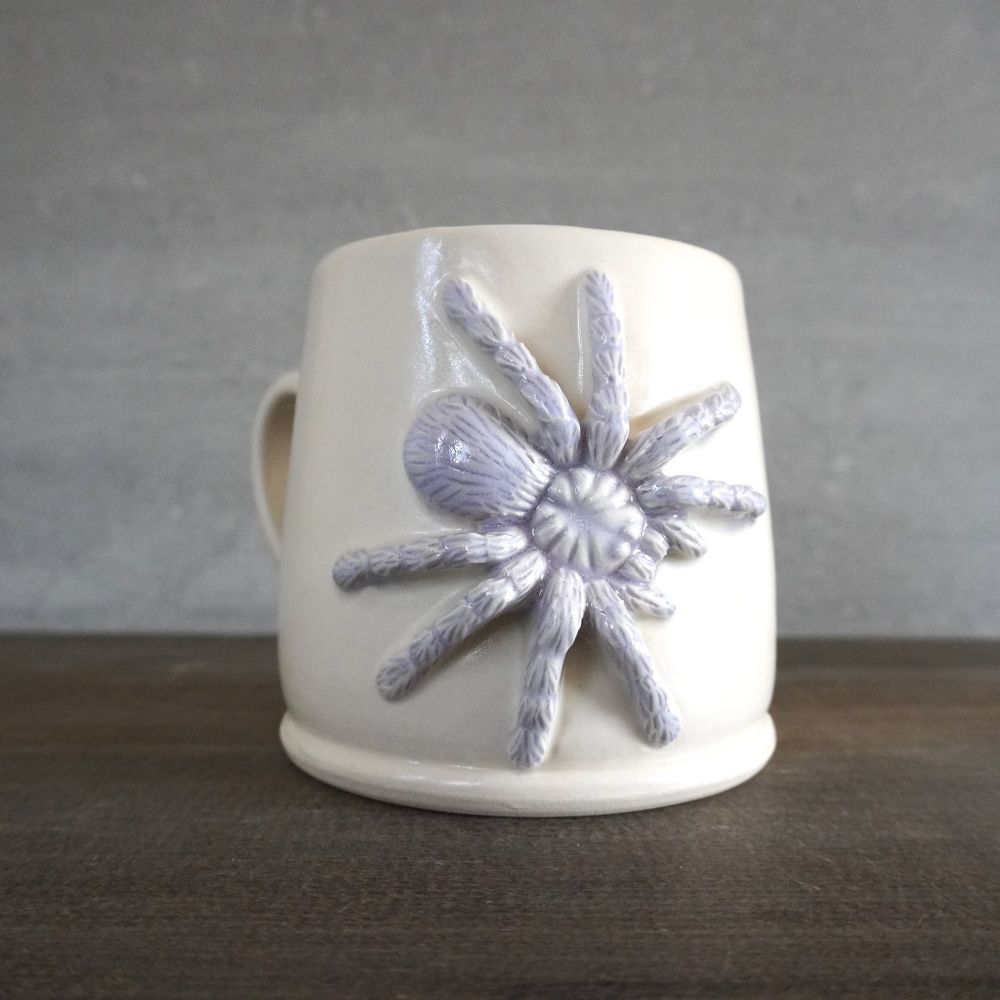 Wheel thrown porcelain mug with a tarantula I sculpted, glazed in a light purple neodymium glaze.