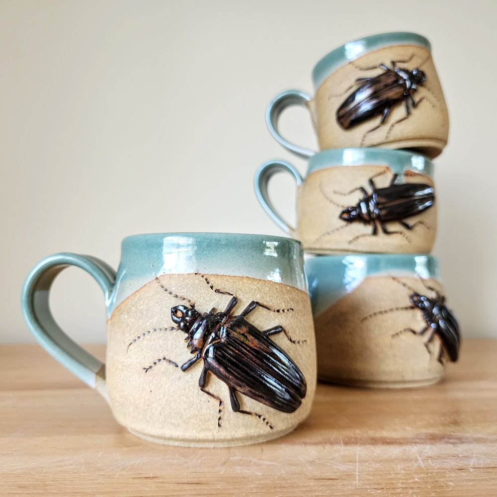 Four wheel thrown stoneware mugs, each decorated with one Palo Verde Beetle that I sculpted and glazed with a black-brown glaze. The top exterior is glazed in sky blue and the bottom is left unglazed.