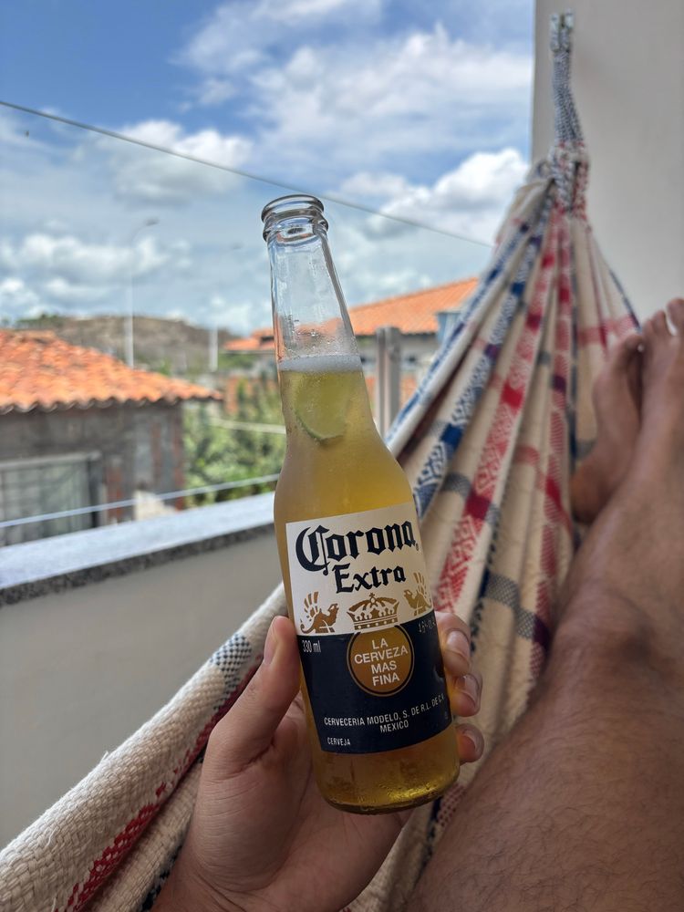 na imagem, as pernas de um homem pardo deitado numa rede, segurando uma cerveja 