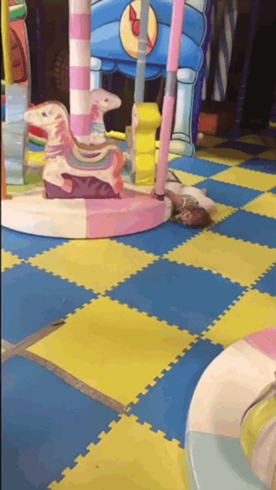 a child is laying on the floor in a playground with a merry go round