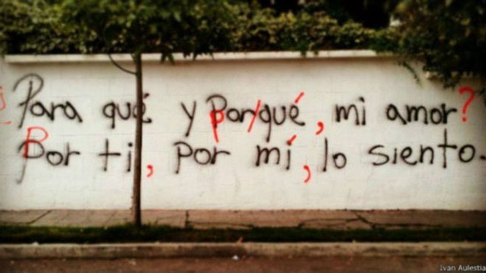 An example of graffiti in Spanish, the black lettering on a white wall having been corrected in red by the vigilante group who have added capital letters, commas and accents as appropriate.