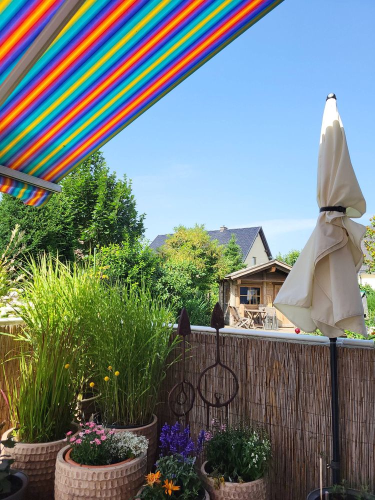 blick von der mit blumentöpfen und gräsern, sonnenschirm, bunter markise u blauem himmel
