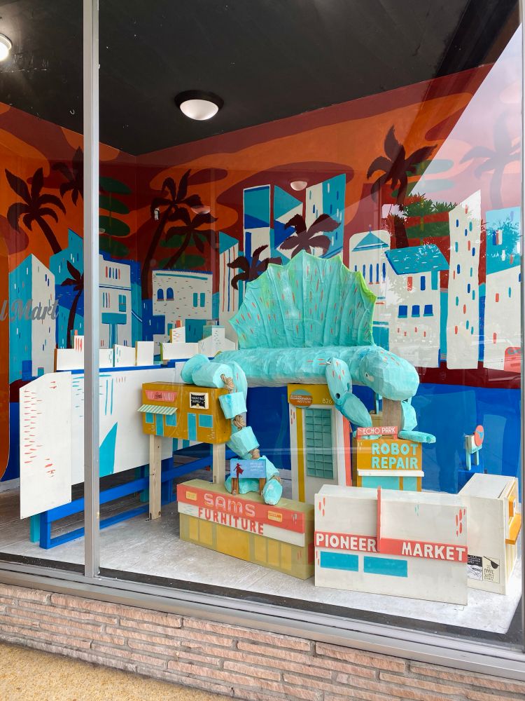 a storefront display of a prehistoric lizard resting on a bunch of blocky buildings.