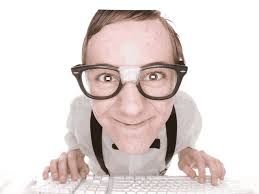 a young nerdy looking boy wearing glasses, a white shirt and suspenders typing on a keyboard while staring directly into the camera at the viewer while noticeably hunched over the desk