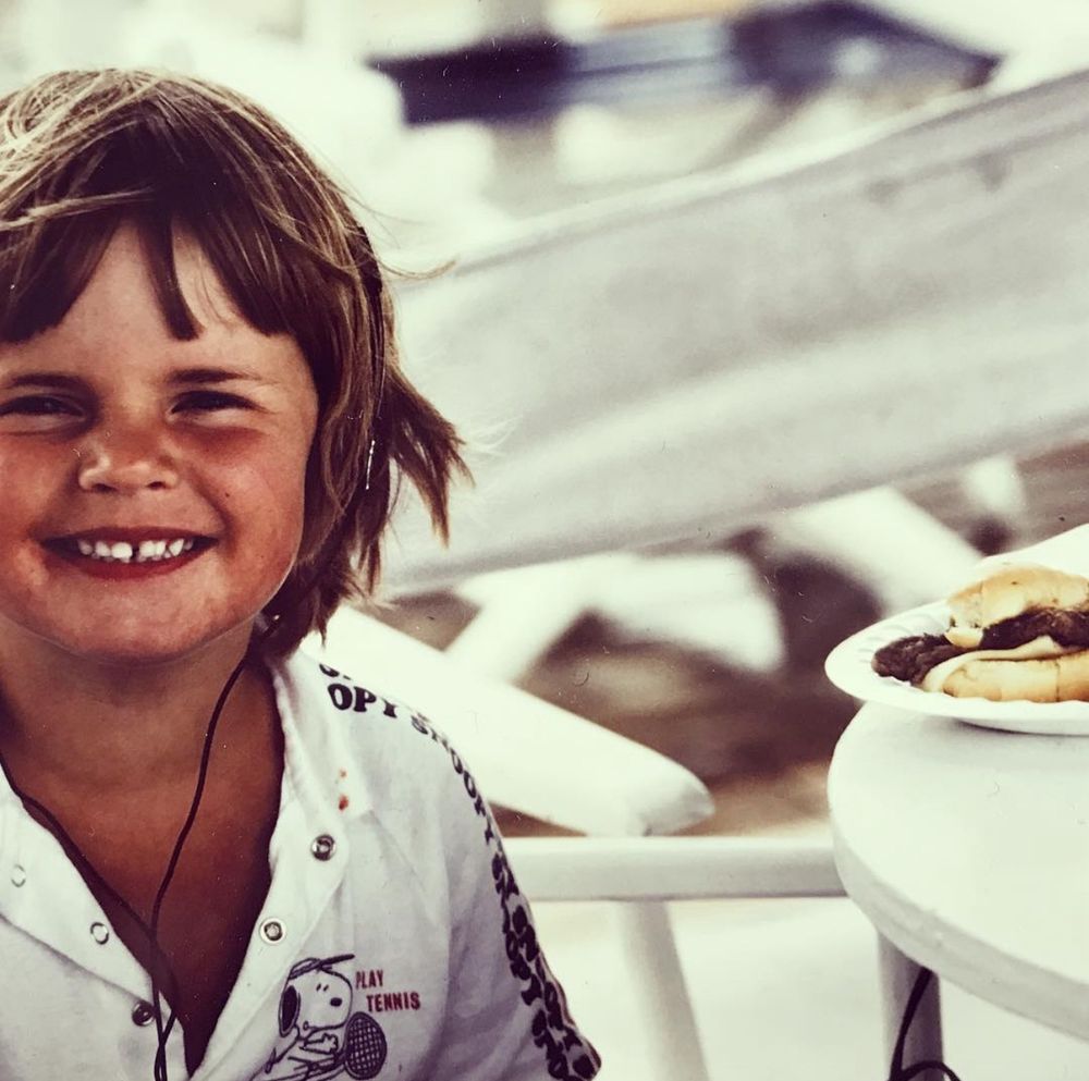 A photo of a kid (me) with short hair, wearing a Walkman with headphones and eating an overcooked but no doubt delicious hamburger 🇺🇸