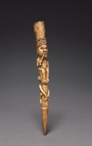 Used by male chiefs, ivory scepters were both symbols of status that indicated worldly authority and religious emblems that suggested supernatural influence. In Yombe society until the early 1900s, the aggressive side of a chief’s authority was dramatized in spectacular public executions. These scepters depict a chief enthroned on the bound body of a criminal destined for such a death. The use of ivory implies that the chief has the fatal power of an elephant. His hairstyle most likely derives from that worn by Portuguese sailors, and he chews a bitter root locally known as <em>munkwisa,</em> administered to persons suspected of witchcraft. A package of various medicines mixed with a resinous material would have been enclosed within the container extending from the figure’s head. Thus charged with potent ingredients, the scepters endowed their owners with specific supernatural powers.