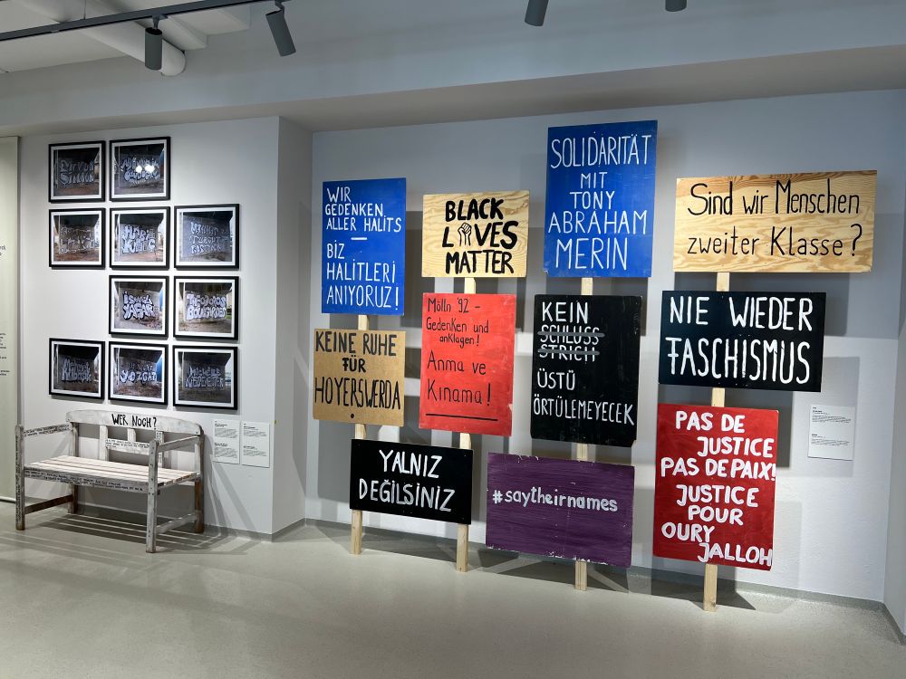 Einblick in die Ausstellung Offener Prozess, an einer Wand hängen verschiedenfarbige Demonstrationsschilder 
