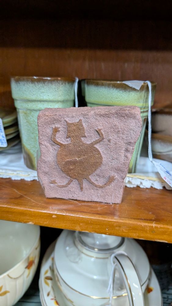 A slab of red stone with most of the face etched away leaving a shape that looks like a fat cat. 