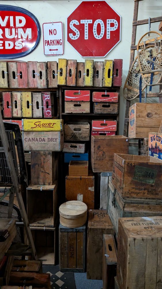 Shelves filled with wood boxes for old glass bottles of soda, beer, and many other items. There is also a "stop" sign and a "no parking" sign on the wall above them. 