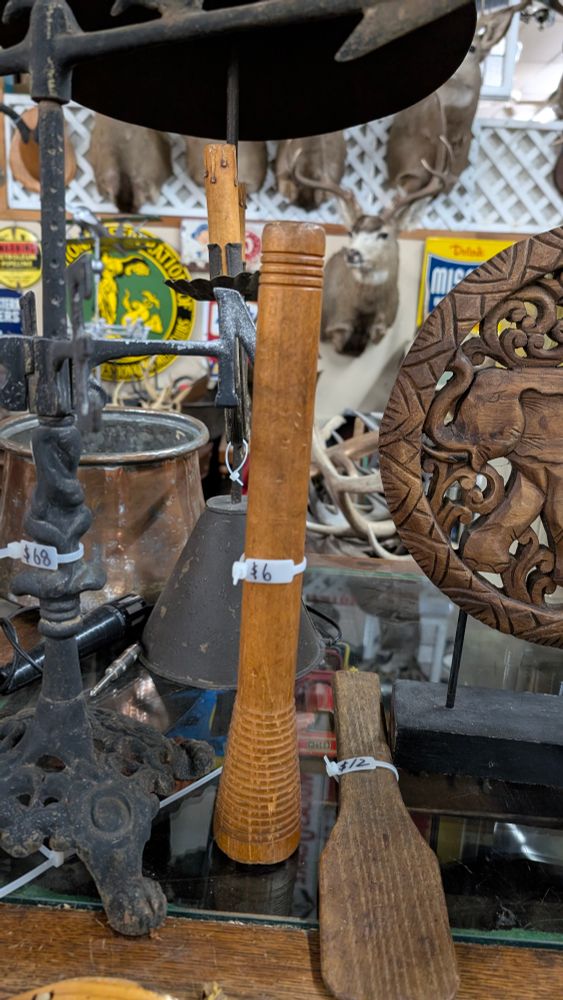 Another wood spool; this one is lighter colored than the last one. There are many things in the background and next to the spool (deer head, wood carvings, metal "things")