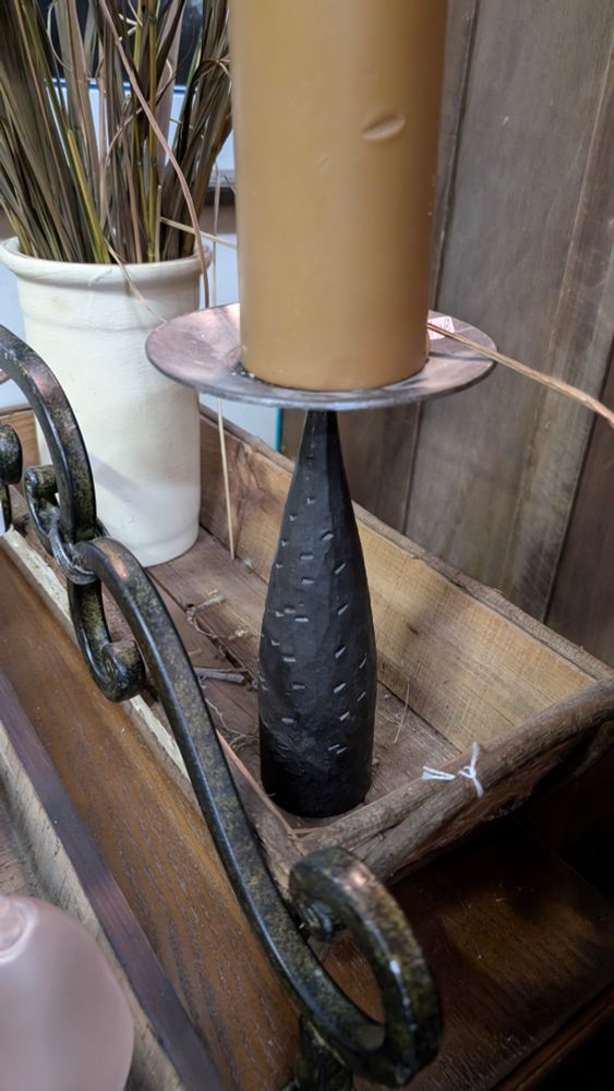 A candle holder with a black base shaped almost like a come and it has notches missing. There is a silver plate at the top with a brown candle on it. 
