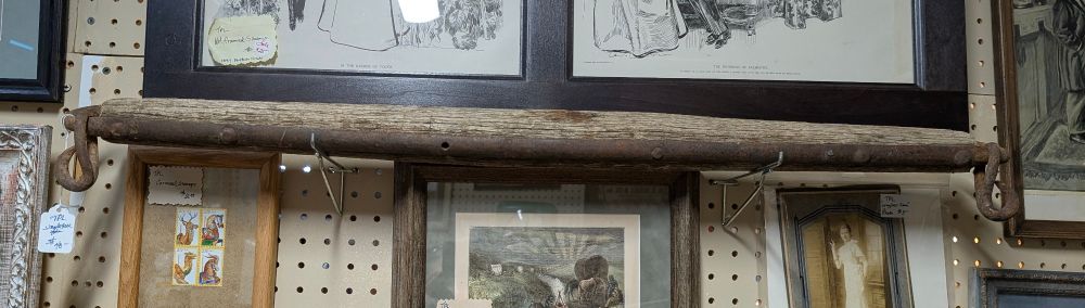 A wood pole with metal on one side and the metal forms loops with hooks at either end. There are picture frames all around it. 