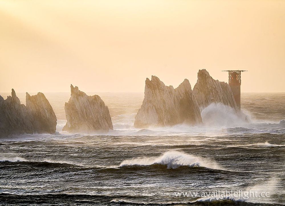 Rough sea and waves crashing against the chalk stacks of the Needles rocks. The lighthouse at the end taking a battering too.
