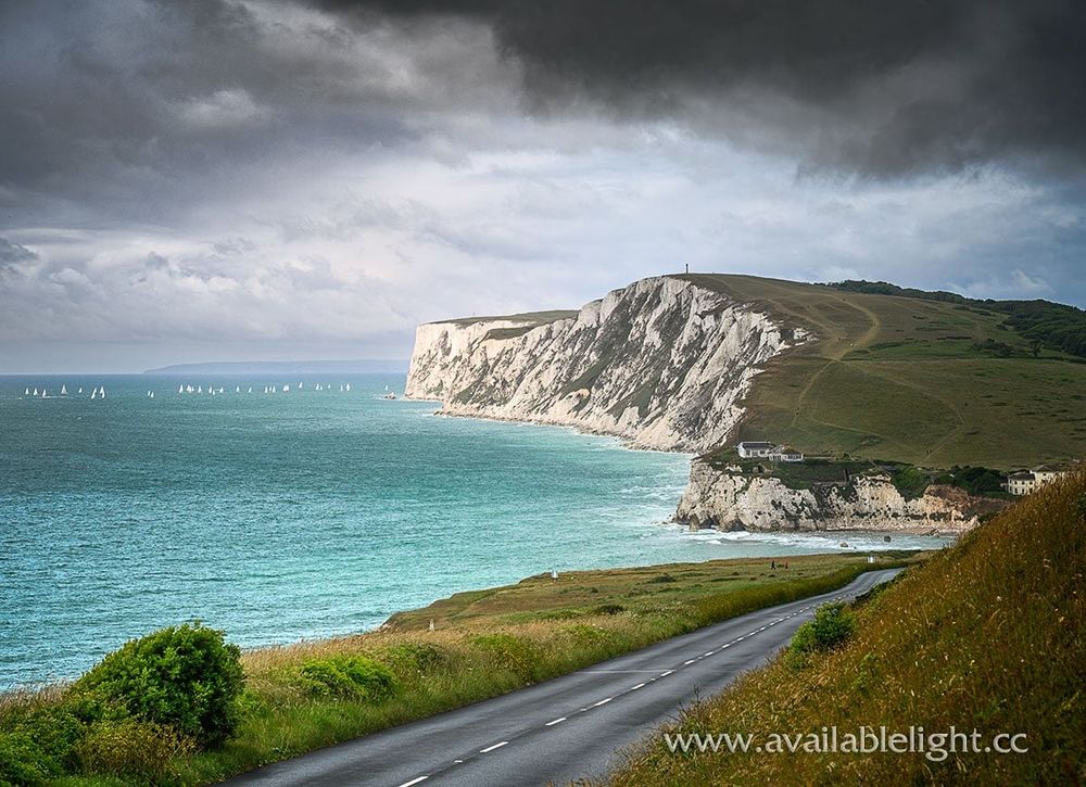 A stormy sky, a chalk cliff, turquoise sea and a few distant yachts
