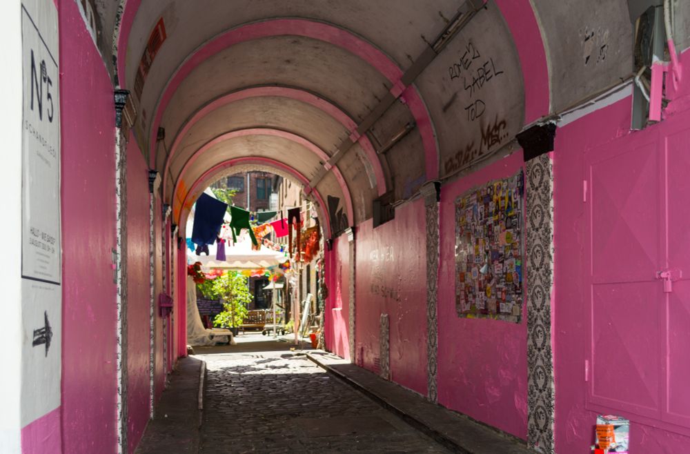 Ein rundbogiger Durchgang, rosa Seitenwände. Am Ende des Gangs ein lichter Innenhof. An einer quer gespannten Leine hängen bunte Wäscheteile. 