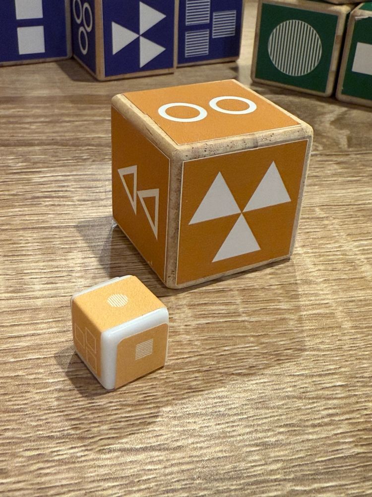 One large cube with strange shapes printed on it next to a smaller cube.