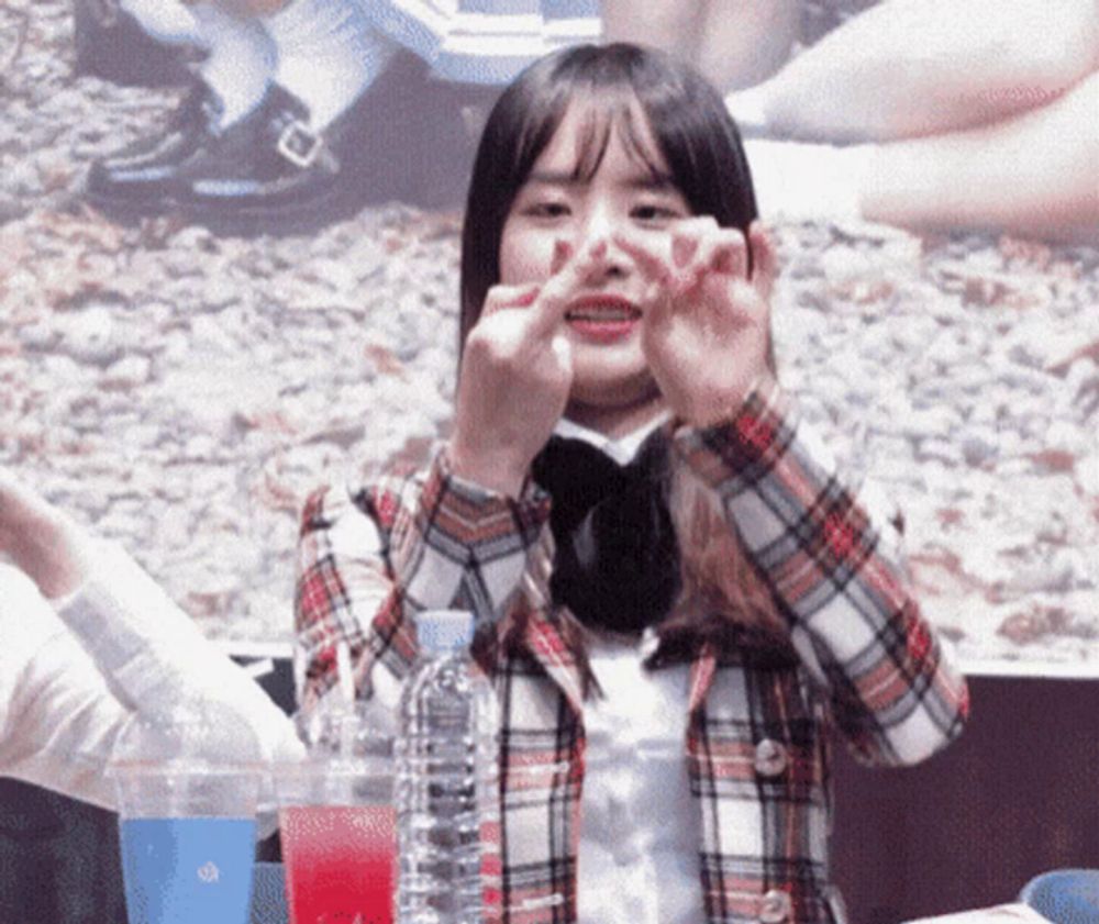 a girl in a plaid shirt is making a heart shape with her hands .