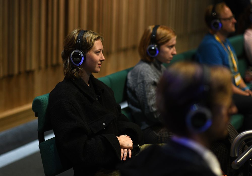 Attendees listening to a presentation through headphones in a conference room setting.