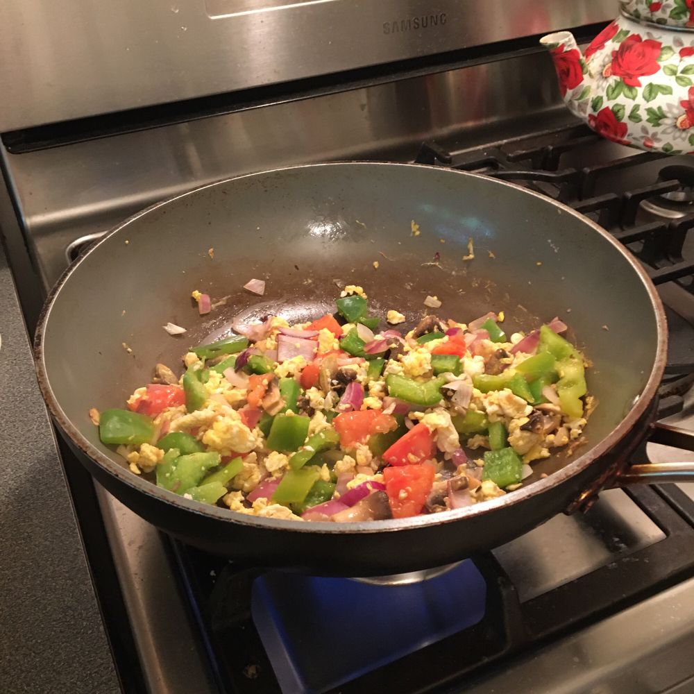 eggs, tomato, mushroom, onion and green pepper frying in a pan on the stove