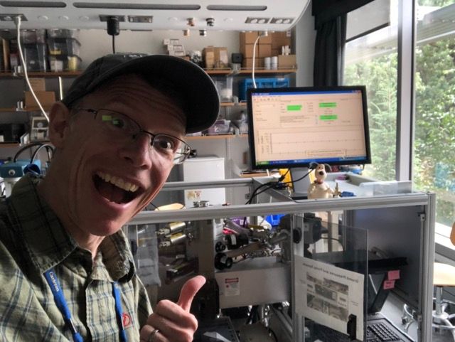 Enthusiastic Nerd in front of an equipment rack with a bunch of science gear and a monitor on top.  A small figurine of Grommit the dog sits on top.
