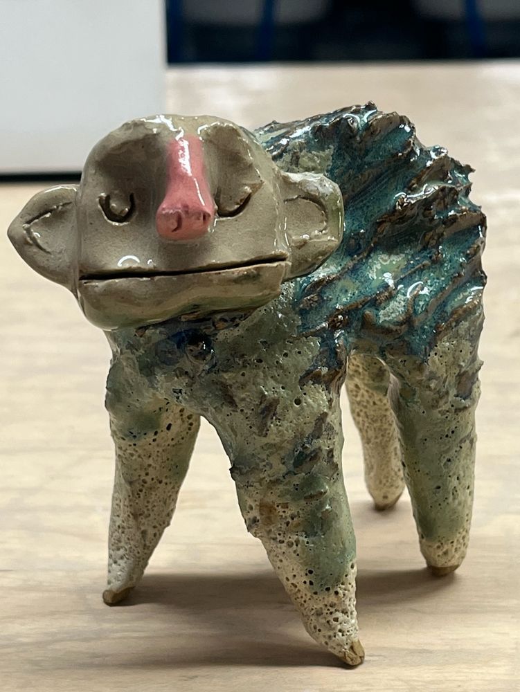 a weird creature with four legs and a humanoid face. it has a wavy back and a wide mouth. its eyes are closed serenely 