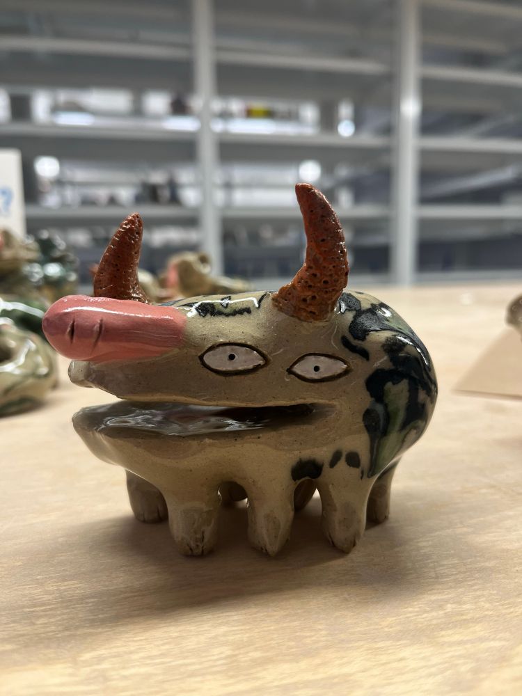 a smiling horned creature with a bunch of legs. on its back are wavy black and green patterns