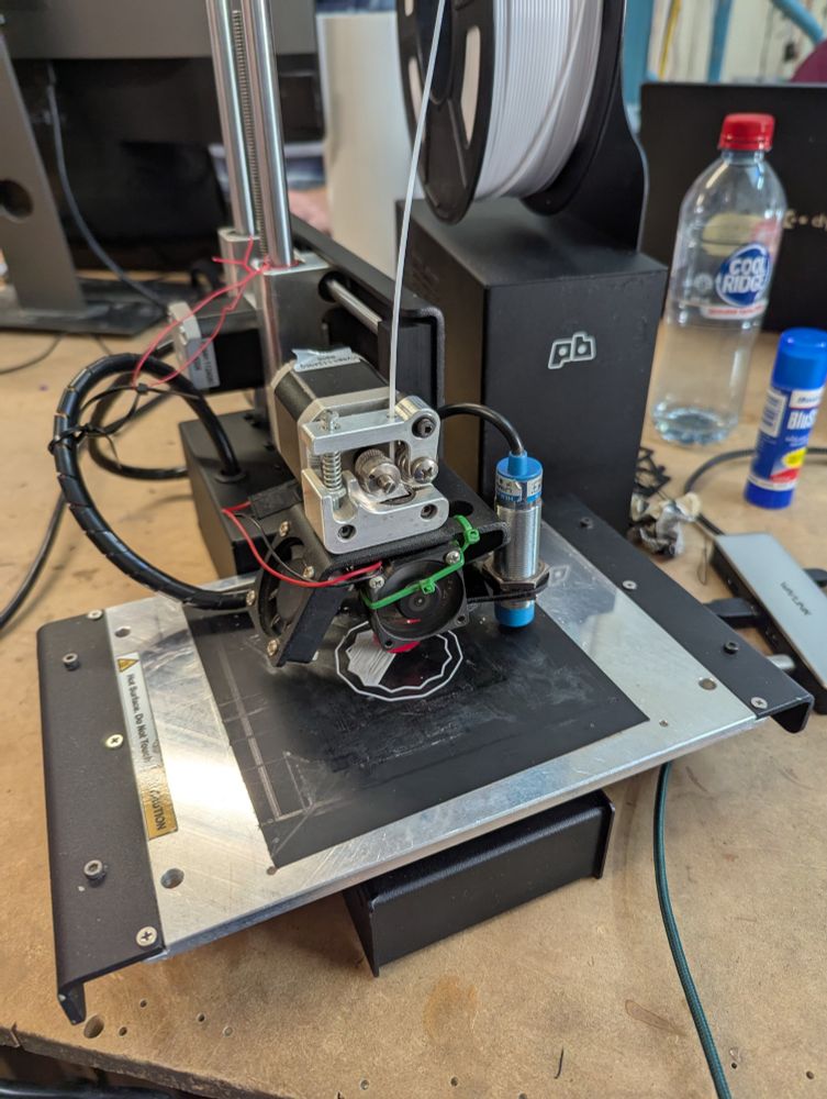 A small black and silver 3d printer printing with white filament. 