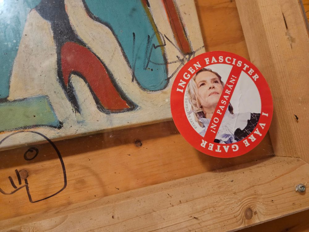 En tund sticker på en vegg med bilde av Ylvi. Det er en rød ramme rundt bildet, og en rød strek diagonalt over. Teksten i det røde feltet er "Ingen fascister i våre gater".