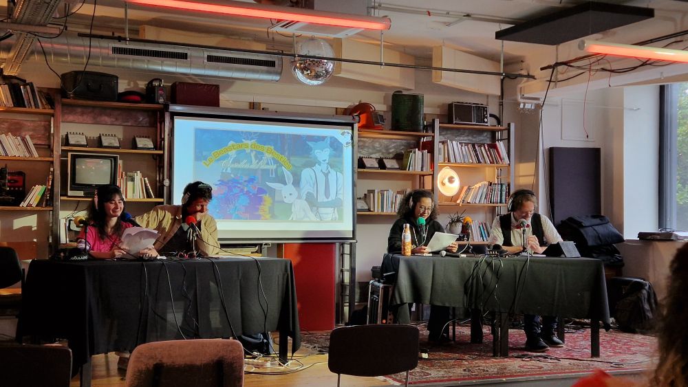 Les animateurices du podcast CalvinBall, lisent leur script sur la scène principale de Podcastres. Derrière eux est projetée l'affiche de leur fiction, un crossover entre Beastars et les Beastie Boys.