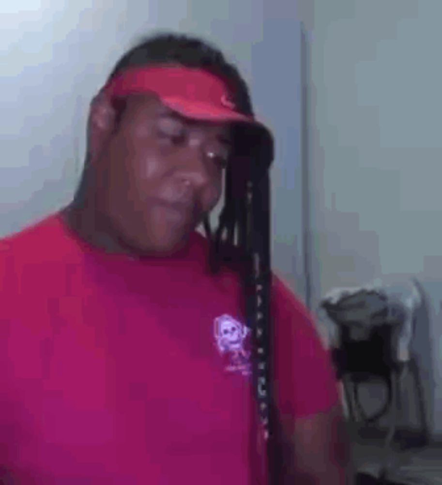 a man wearing a red shirt and a red hat with dreadlocks is looking down .