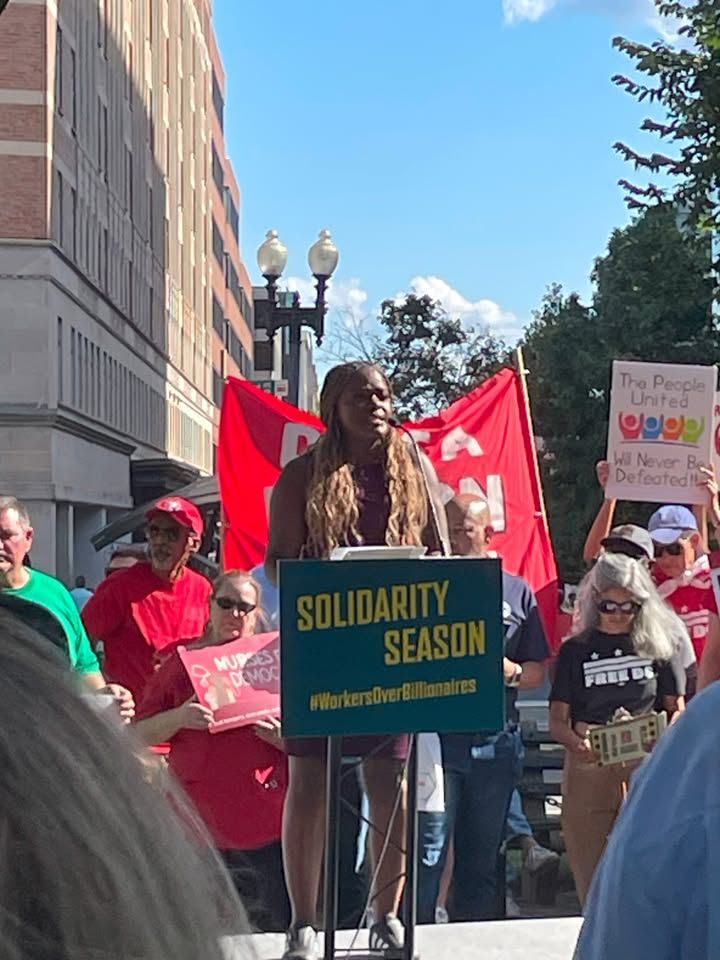 Person speaking at a rally with signs reading 