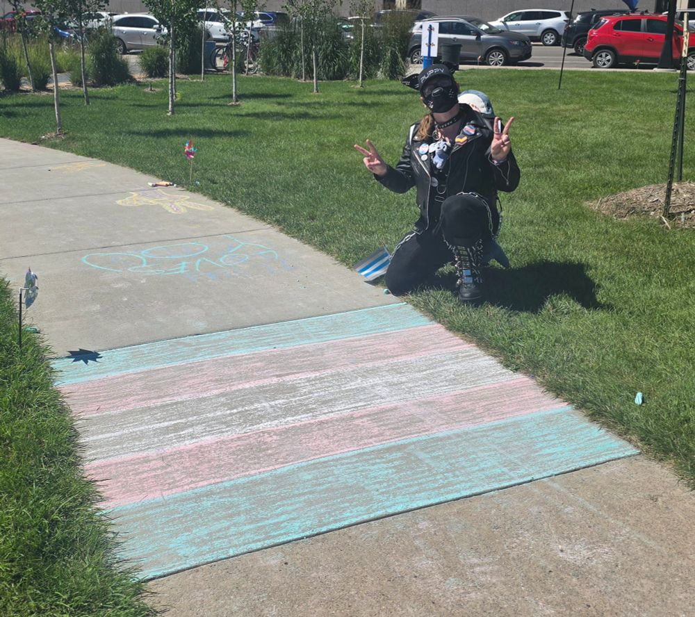 Me kneeling by some trans flag chalk on the sidewalk