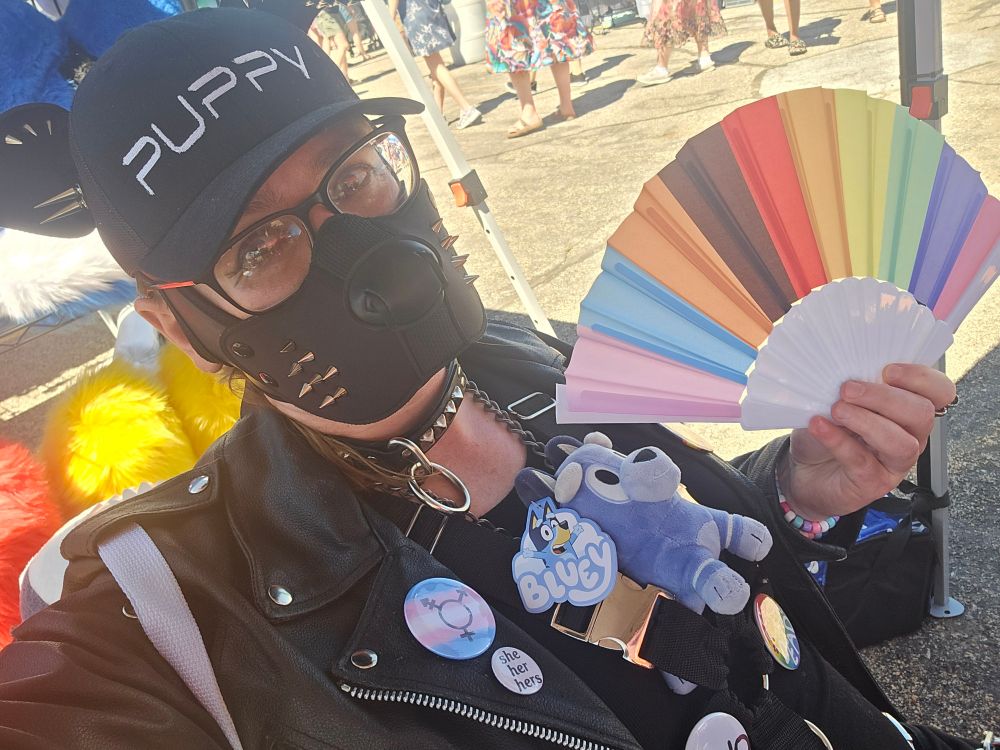 Me holding up one of the pride flag fans that was given out. Noticeably have a small Socks plushie sticking out of the top of my black nylon harness