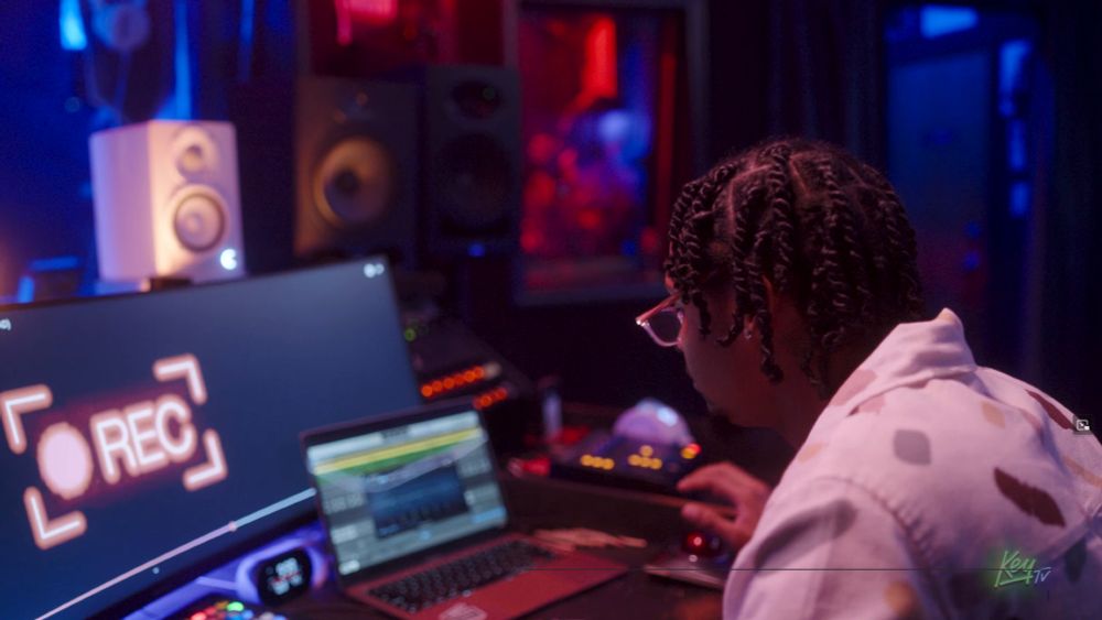 Screengrab of a tv show featuring a black man with twists in a "audio recording studio"