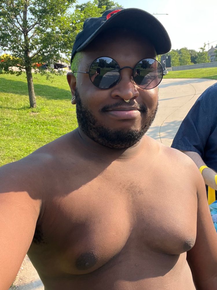 Shirtless selfie of me wearing a black hat and black circular sunglasses. 