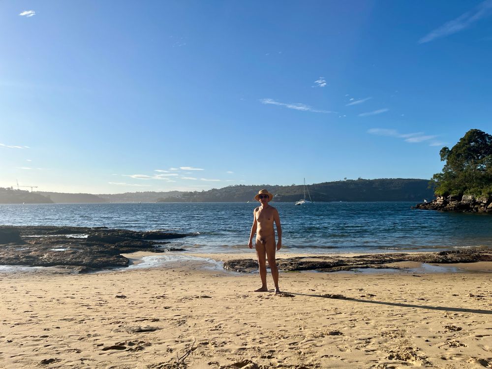 Man standing at a beach, his body is partly shadowed due to the position of the sun. Blue skies. 