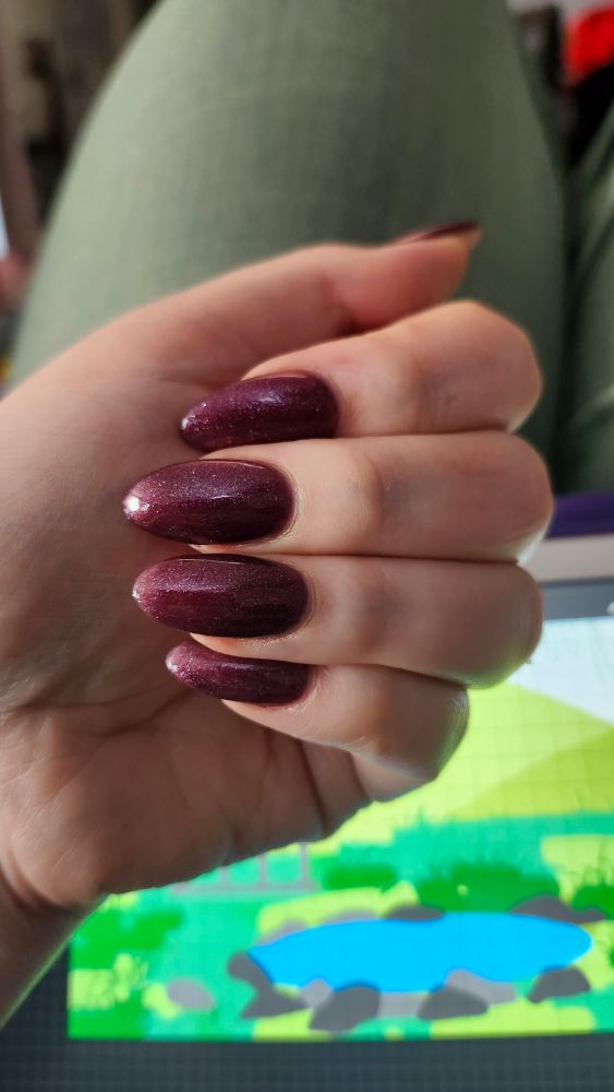 A hand curled to show off a deep berry red glittery nail polish