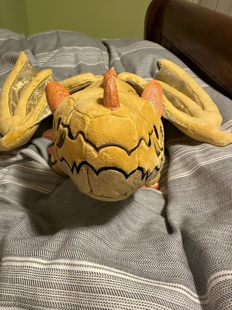 A gold weighted dragon plush looking directly at you from Weighted Wonders.