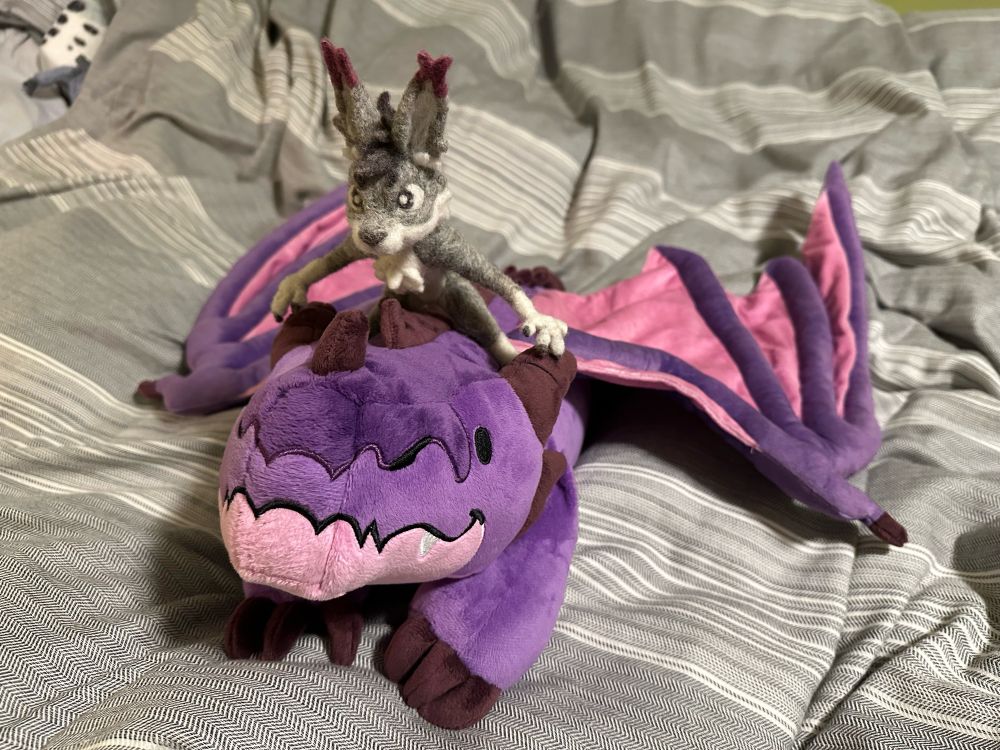 A needle felt figurine of Tealo the lynx riding a purple warm-able dragon from Weighted Wonders.
