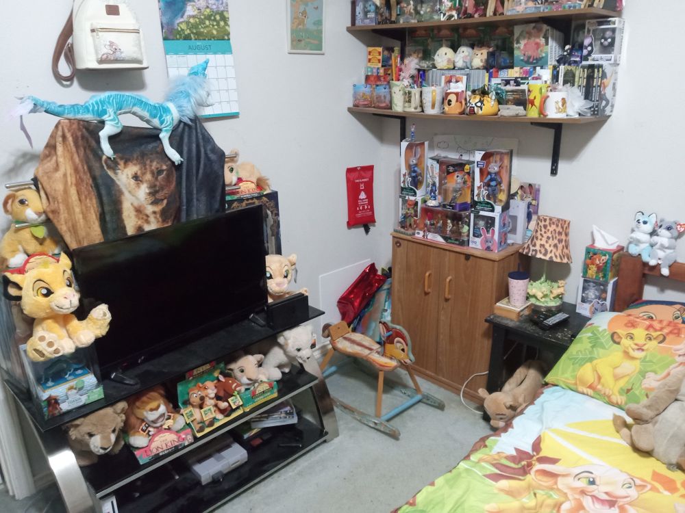A tv adorned with lion king merch, a Bambi  makeshift rocking gkrze beside it, and shelves of Disney toys and merch.