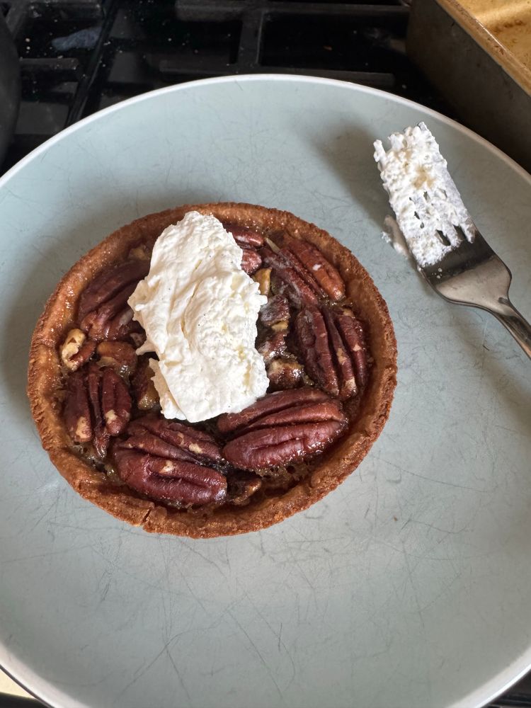 A miniature pecan tart that is on a plate and topped with a dollop of whipped cream 