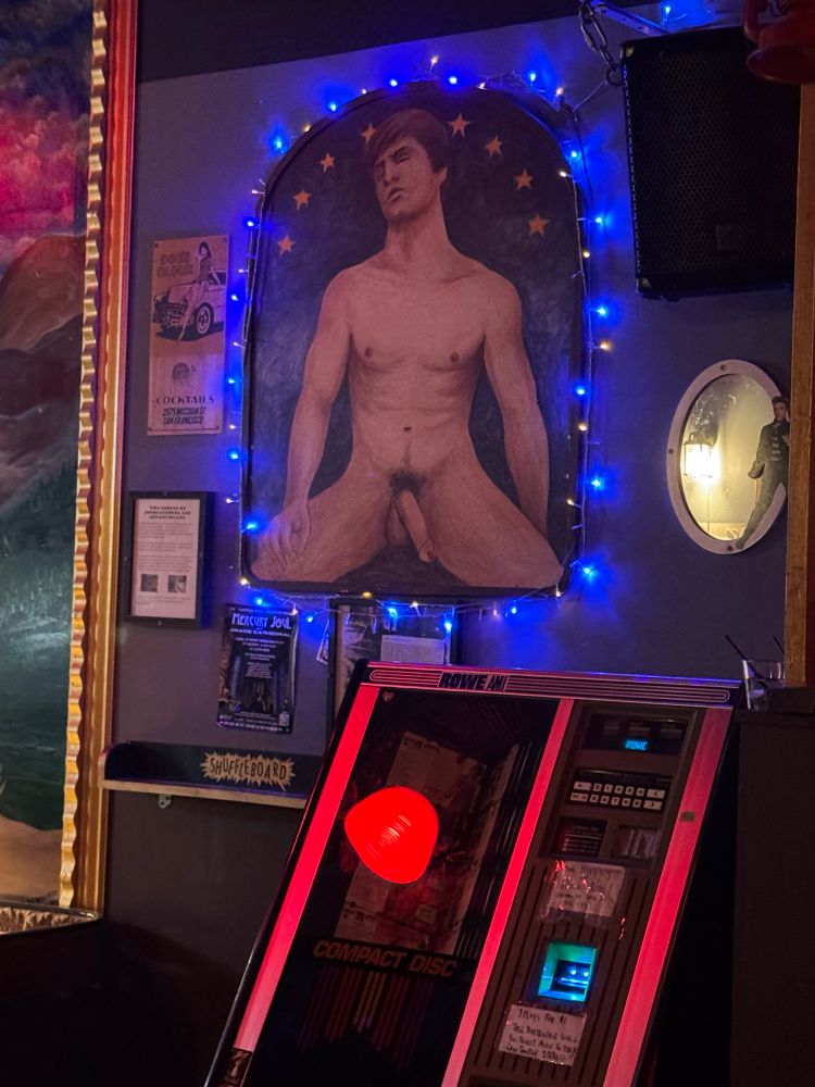 A painting of a naked man hangs above a jukebox in a bar